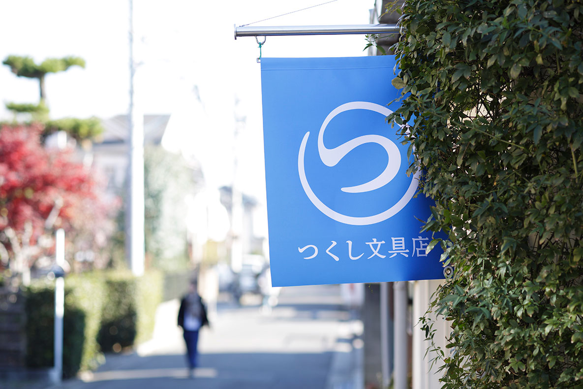 国分寺第三中学校前の住宅街で青い「つくし文具店」ののれんが風になびいている。